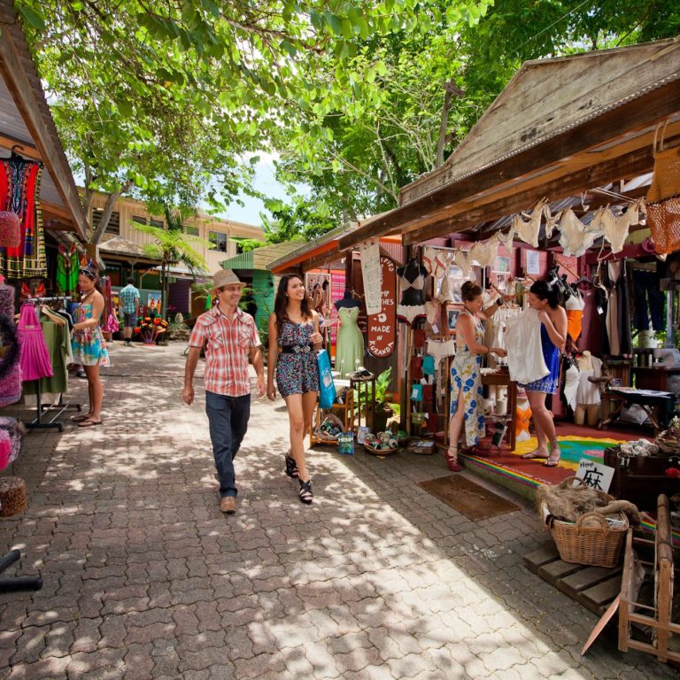 couple walking down paved walkway with colorful clothing markets on each side