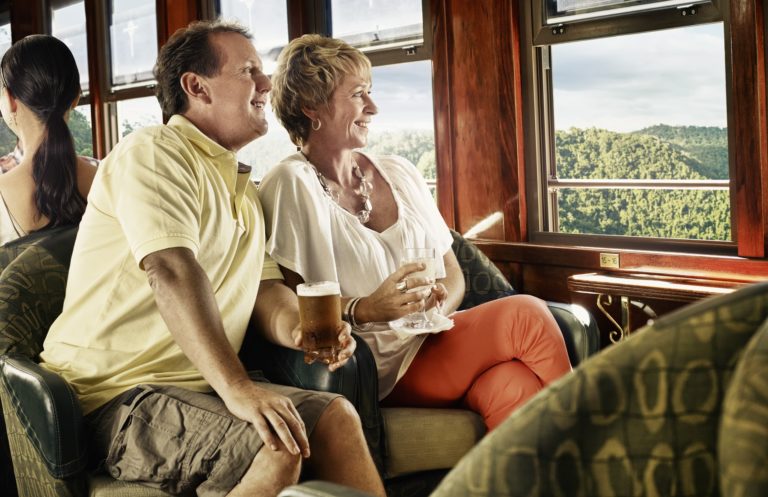 Couple sitting in lazy boy chairs with an alcoholic drink looking at the view out the train window