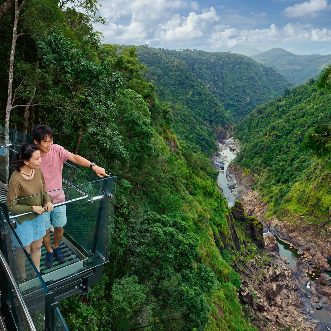 couple standing on the glass section of the edge lookout at barron falls high above barron gorge