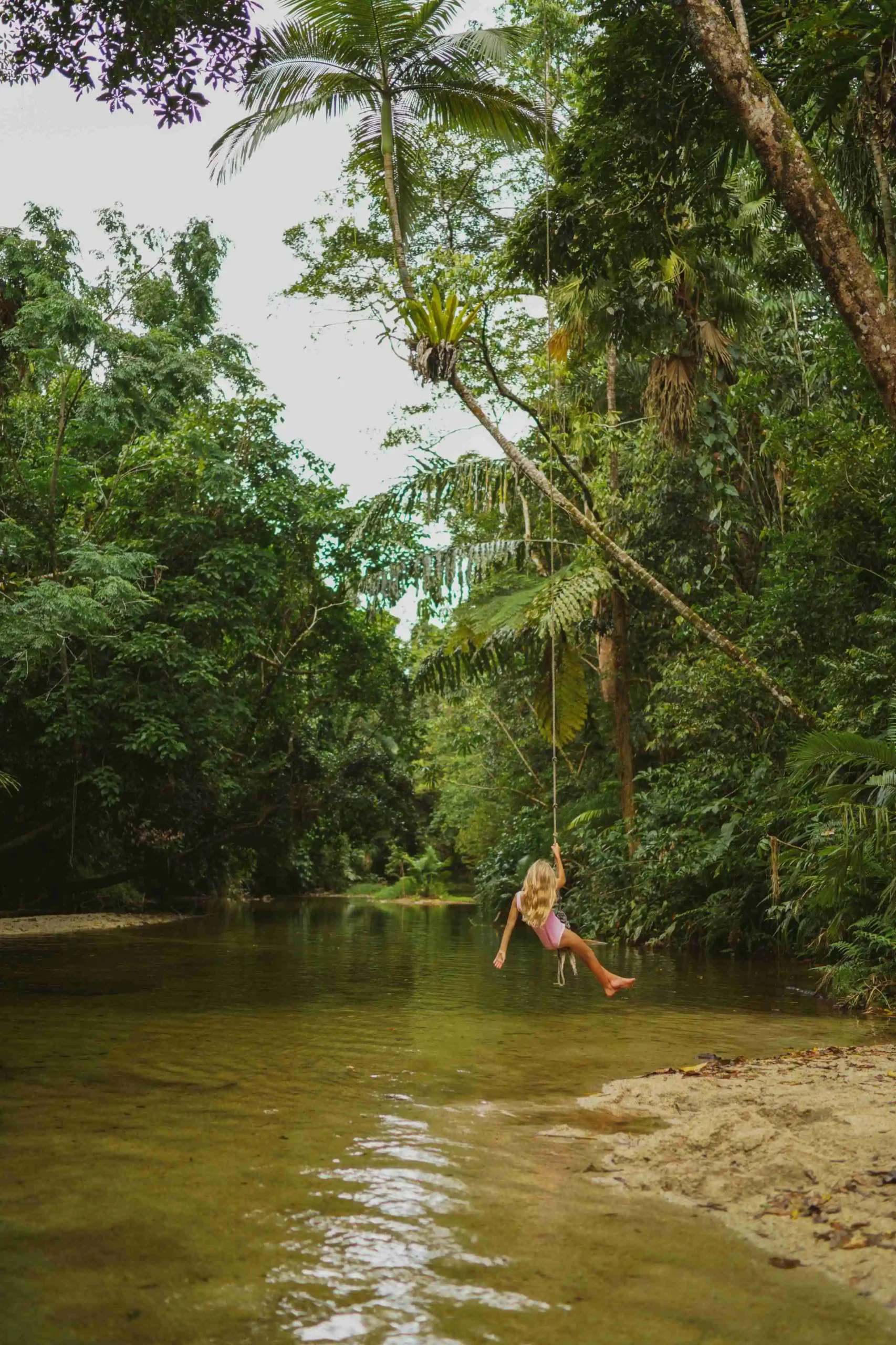 Child on tree rope swing over creek