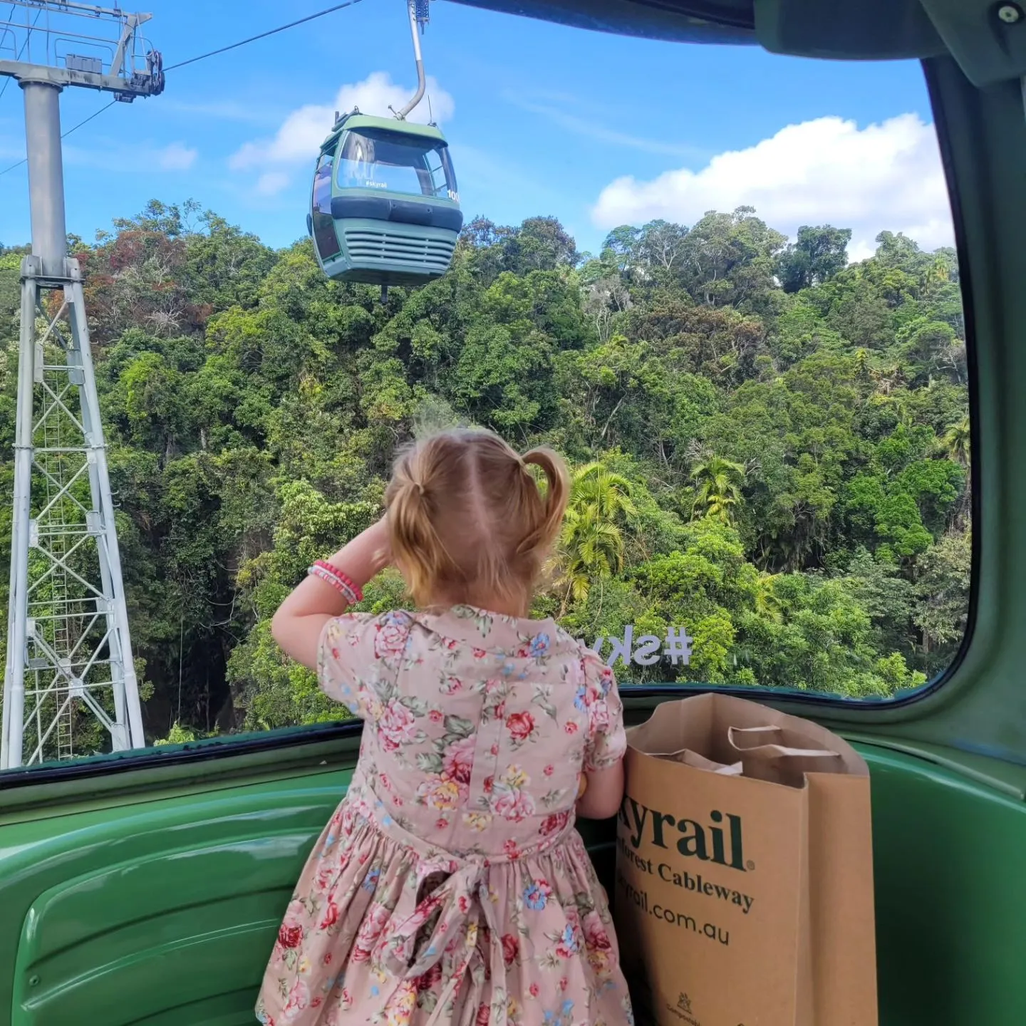 The back of a small child watching out the window at skyrail gondolas passing by