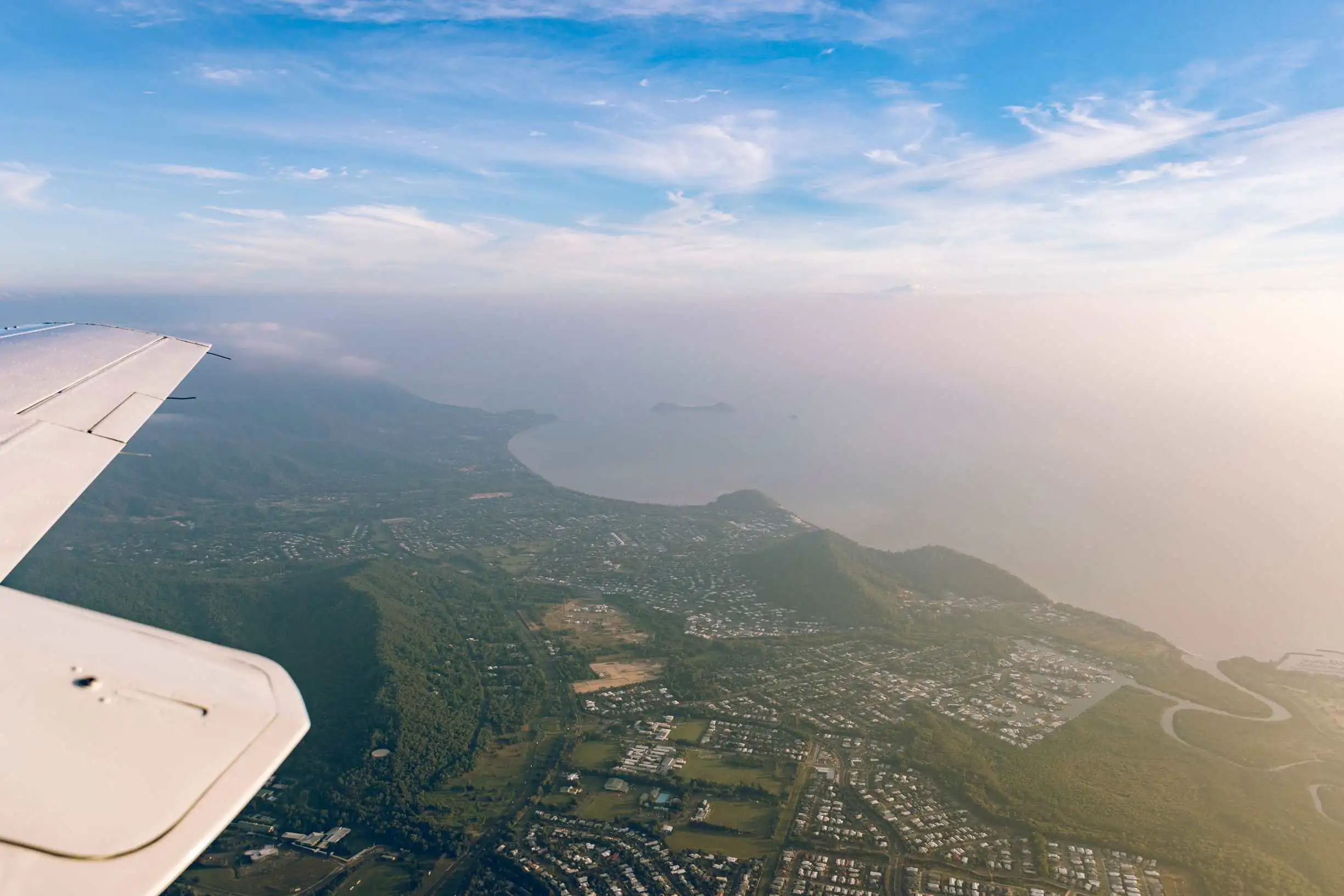 The view from a plane when arriving in cainrs. The wing top and below the city surrounded in deep greenery meeting the ocean.