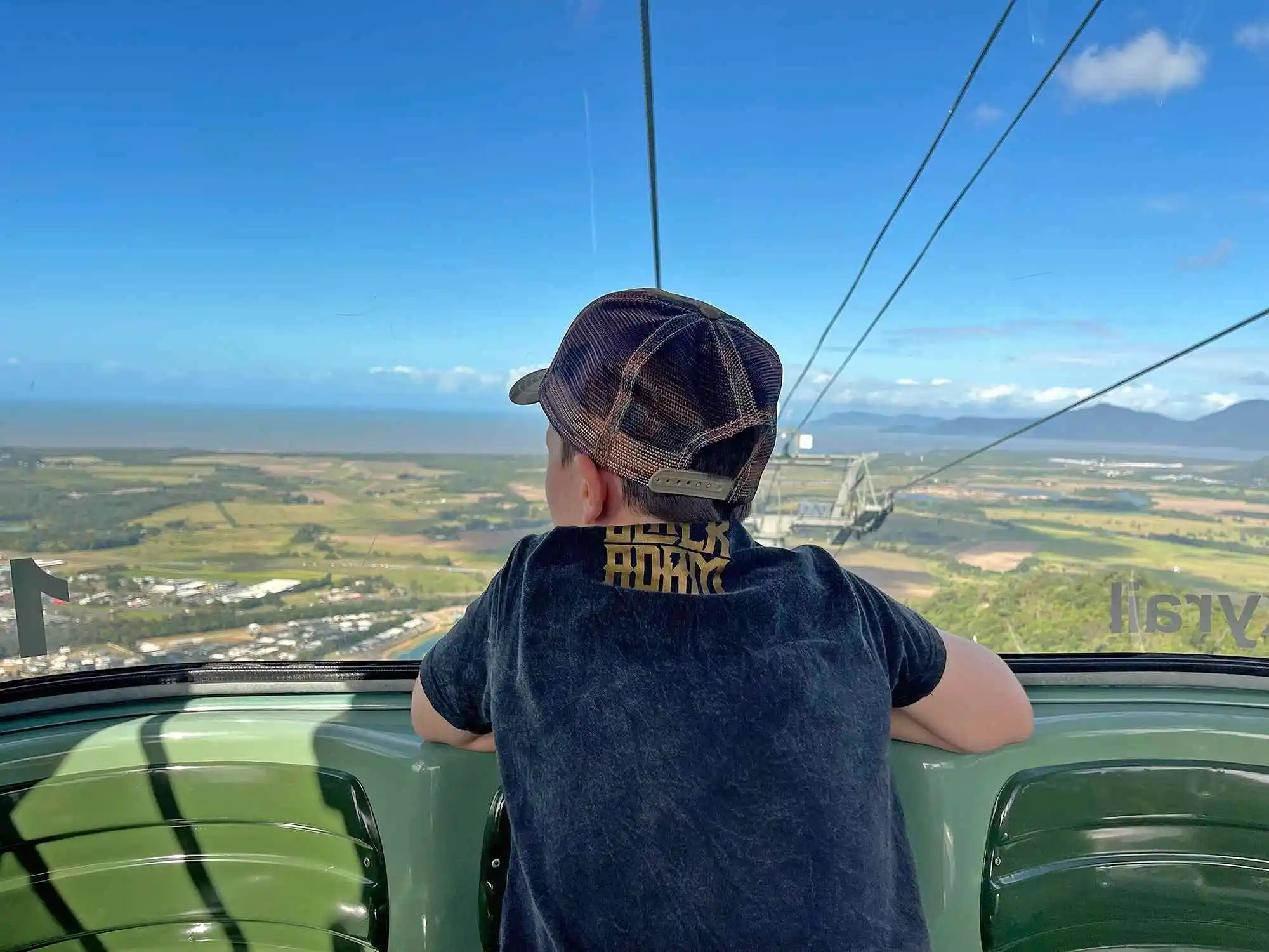 The back of a boy looking out of a gondola window at the bright blue skyline.