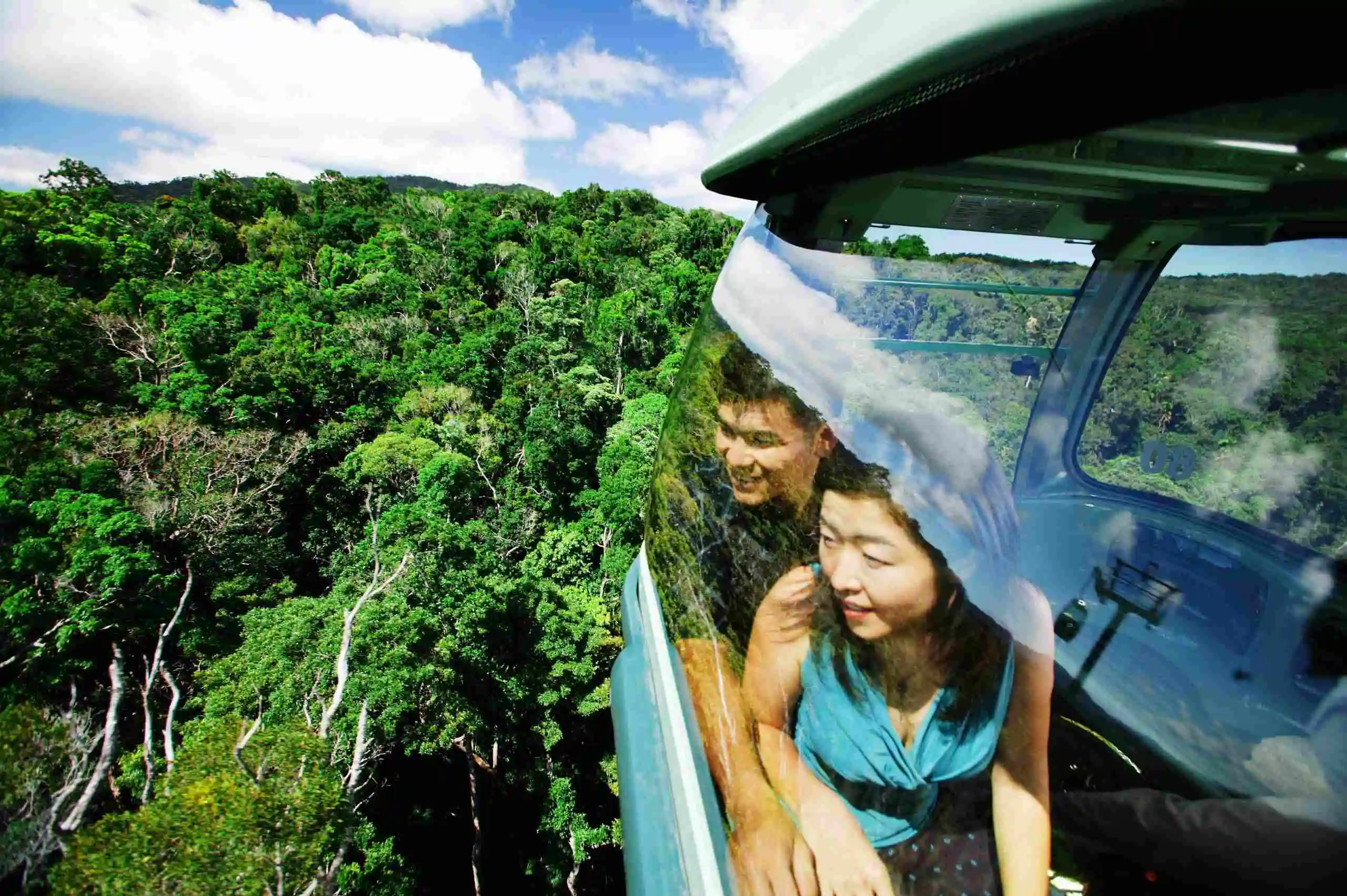 Side view of two people look out the side window of a gondola as they glide just above the rainforest canopy. CTrip