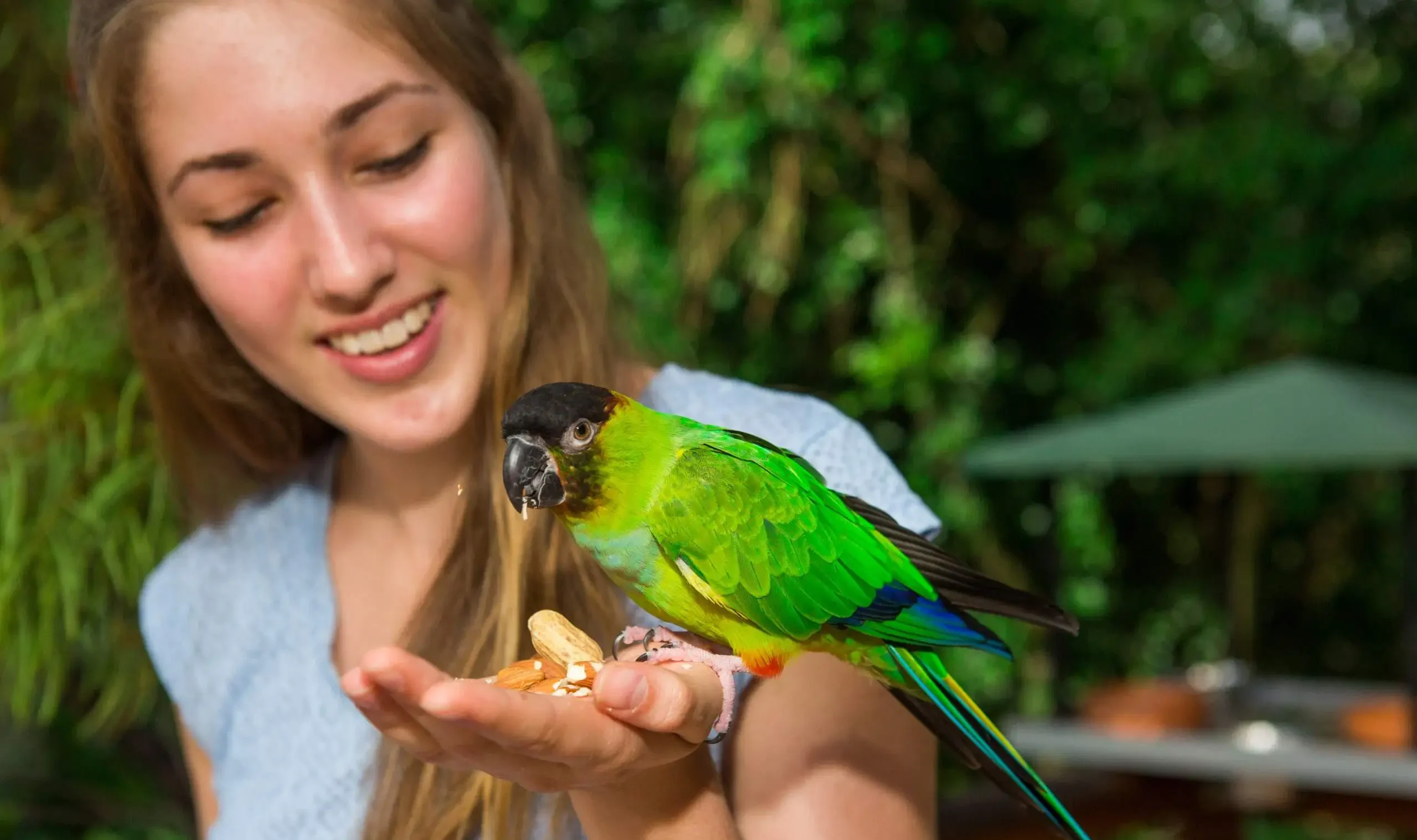 A girl smiles at a green bird sitting on her hand