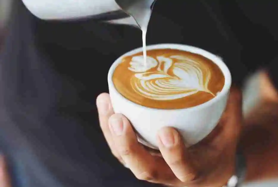 looking down as a barrista makes a flower with milk in a white coffee cup