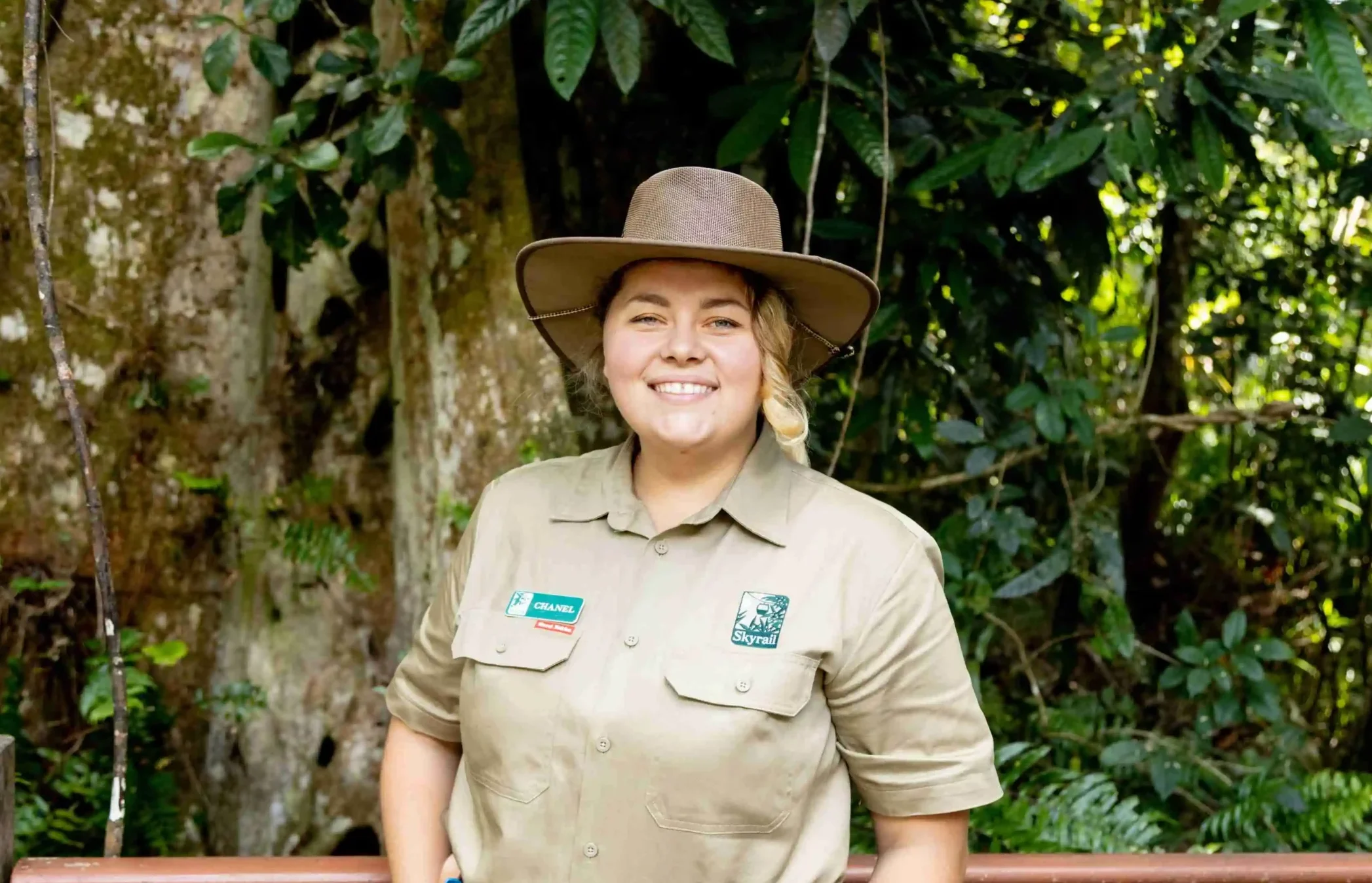 Skyrail Ranger Chanel stands smiling at the camera with rainforest behind her