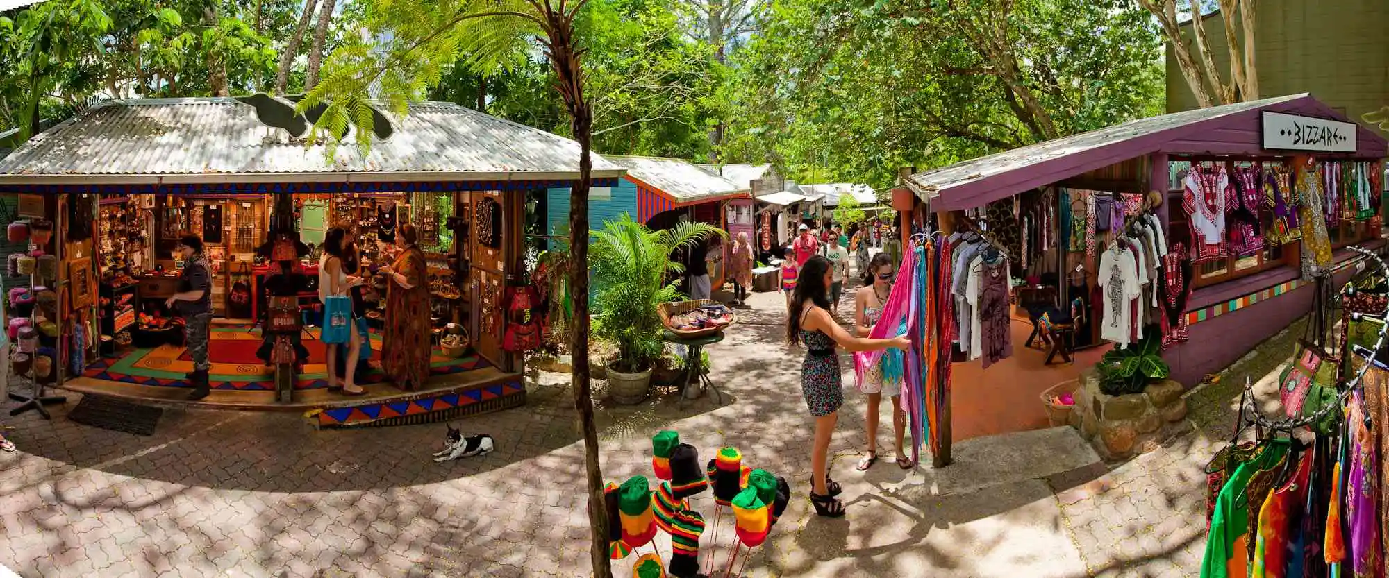 A wide lens image of the colourful wooden Original Kuranda Markets. Two girls looking at a shop.
