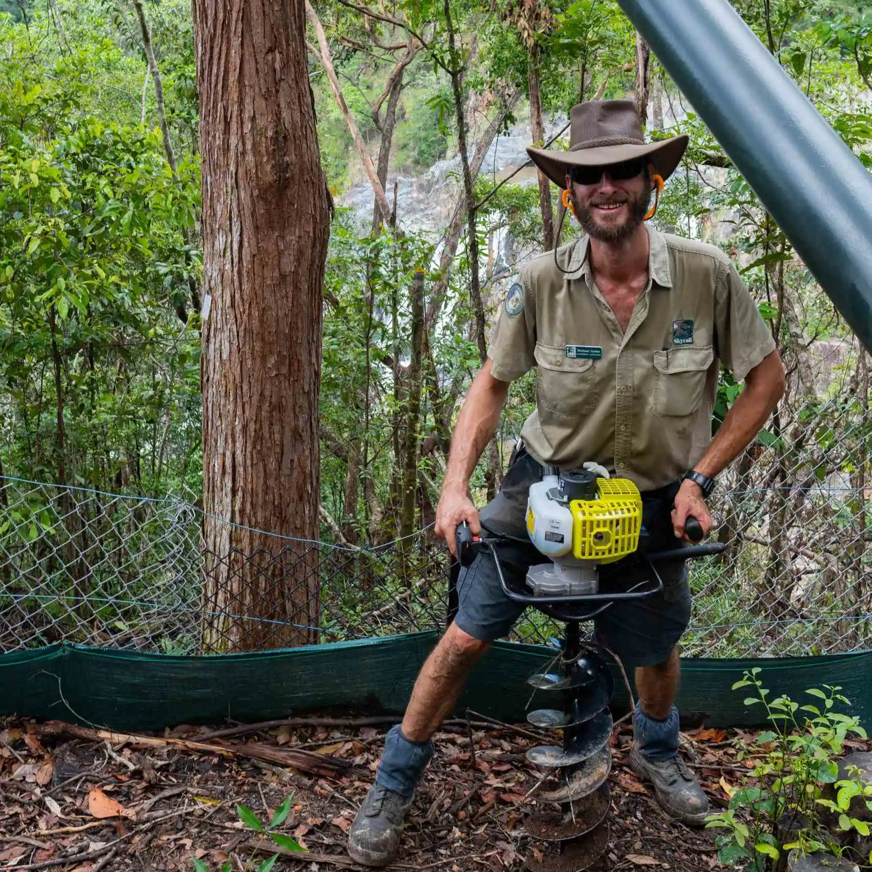 A Skyrail Ranger uses a machine to dig holes for revegetation of the rainofrest