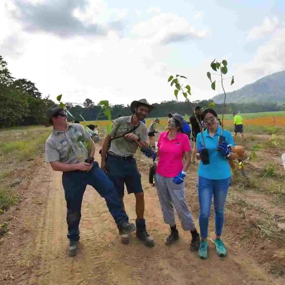 Two male rangers and two females stand laughing with each other with trees in their hand ready to plant