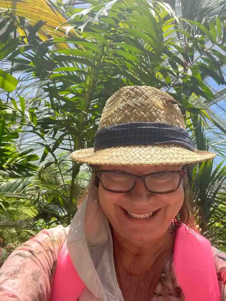 A lady smiling at the camera with a butterfly sitting on her straw hat