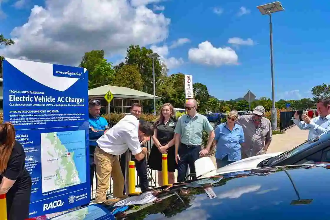 A group of people gather at an electric vehicle charging station 