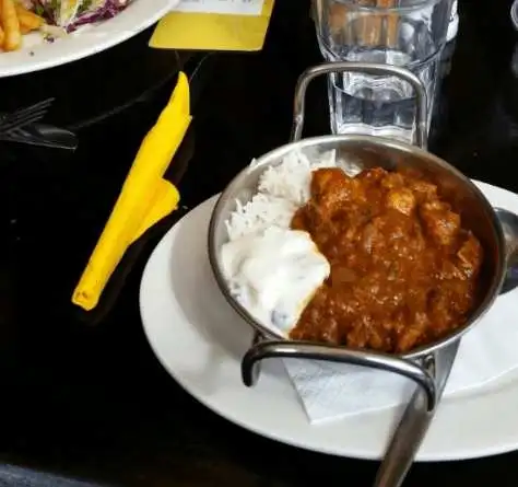 Curry and rice in a silver bowl sits on a plate and napkin upon a wooden table