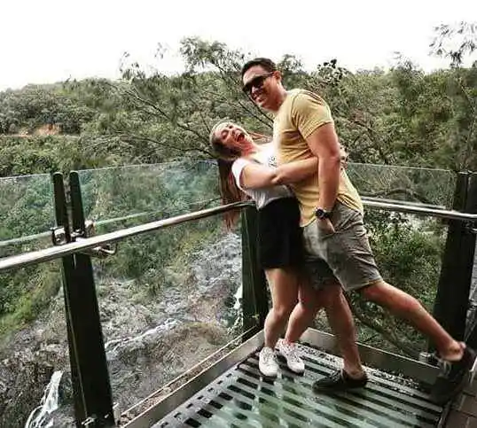 A girl hugs a man at a glass lookout to the Barron Falls