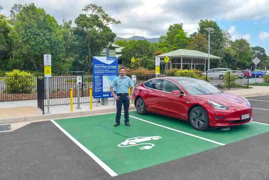 A Skyrail staff member stands at an electric vehicle while it charges in the electric vehicle park