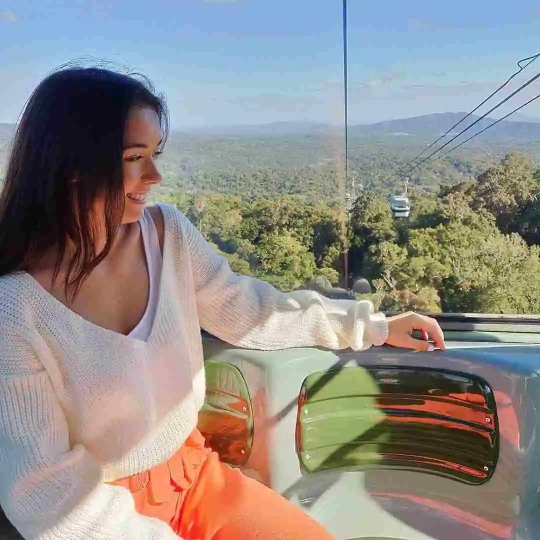 A girl sits side ways looking out of a gondola window across the Barron Falls National Park